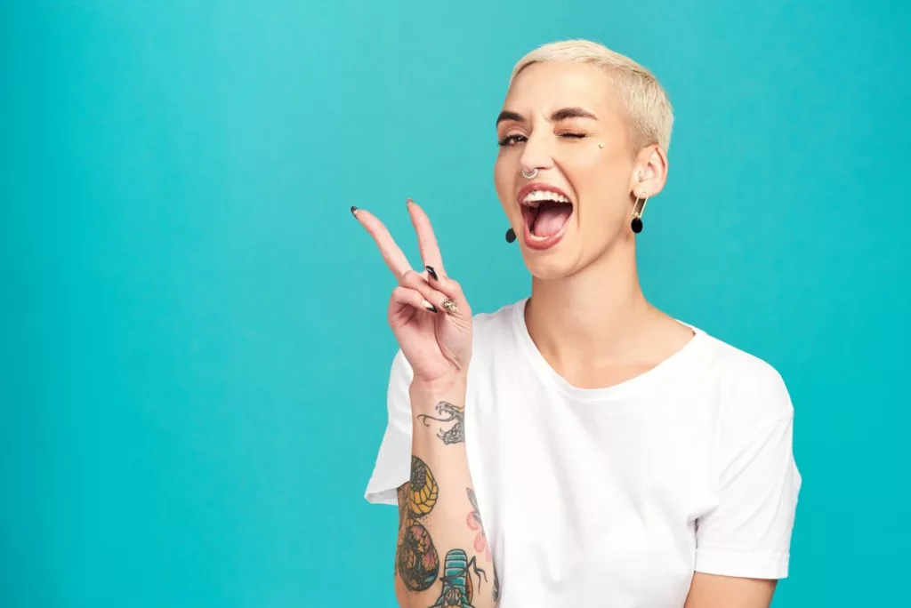 Woman with tattoo on arm making peace sign feeling happy about the help she gets in the Prince's Trust.