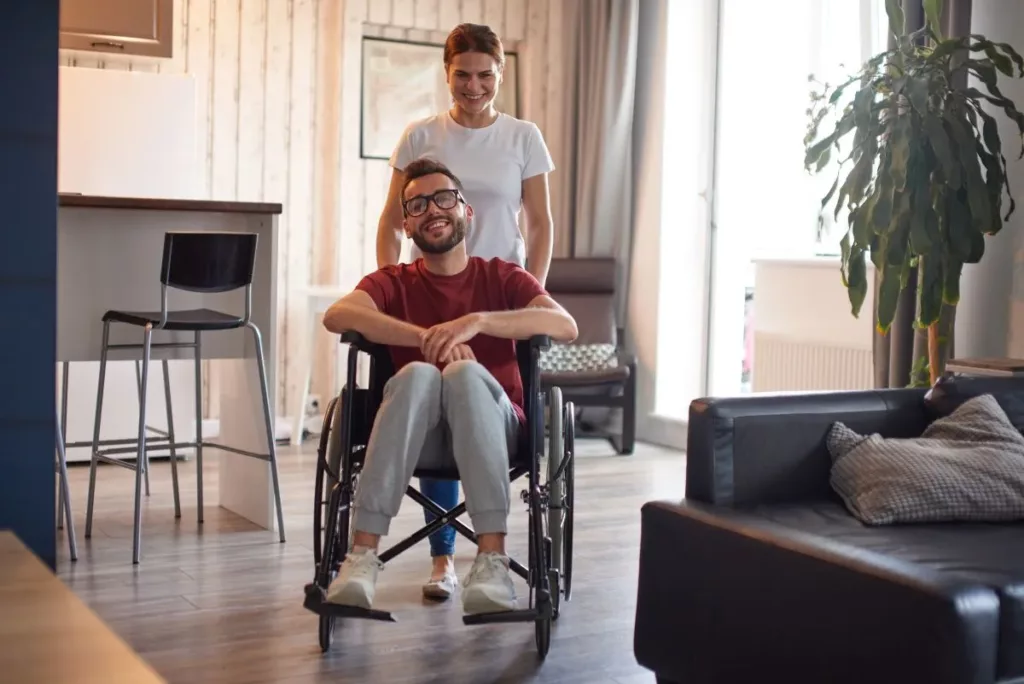 A man who has had his disability registered is sitting on a wheelchair while he is being pushed by a young woman.